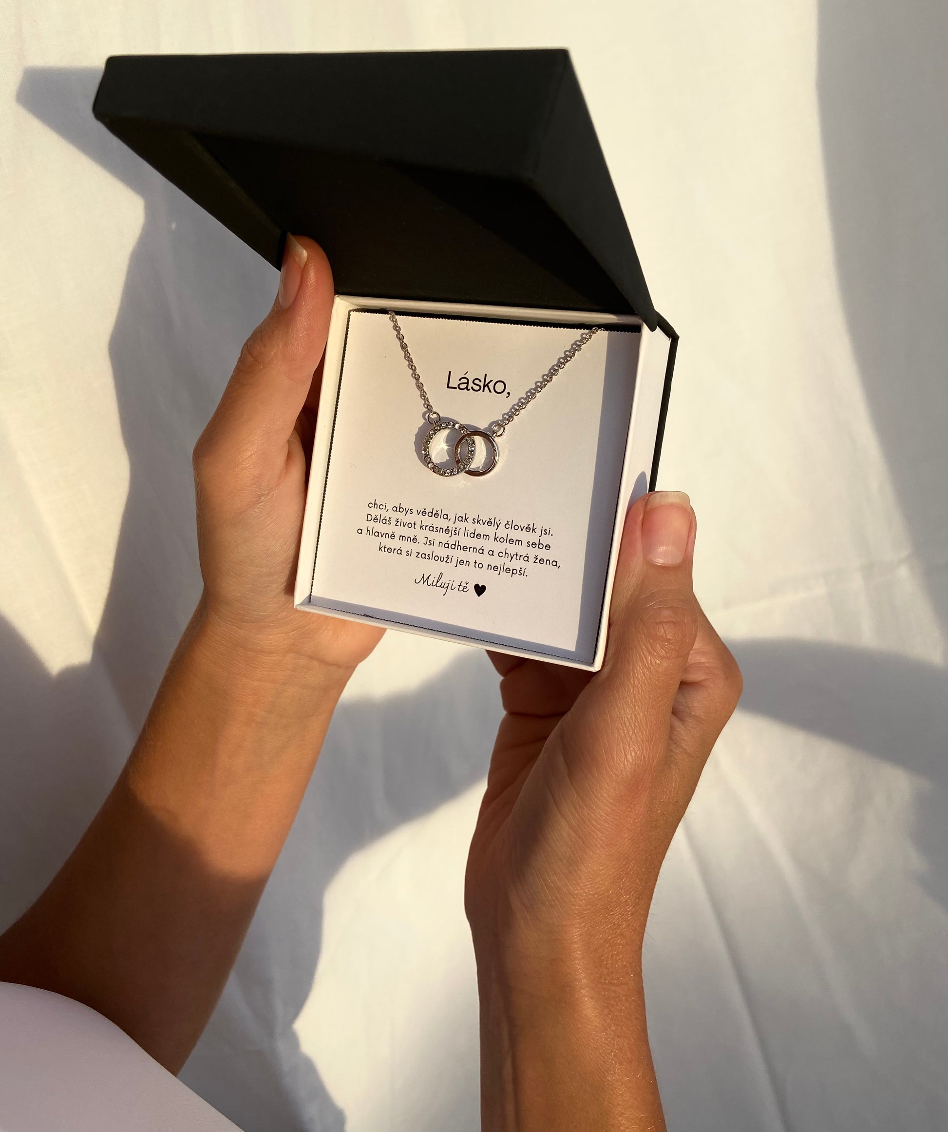 Personalizovaný stříbrný náhrdelník se zirkony ve tvaru spojených kroužků se vzkazem pro přítelkyni, držený v rukou modelky 